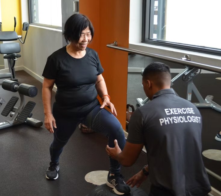 Exercise Physiologist guiding older client through leg exercise